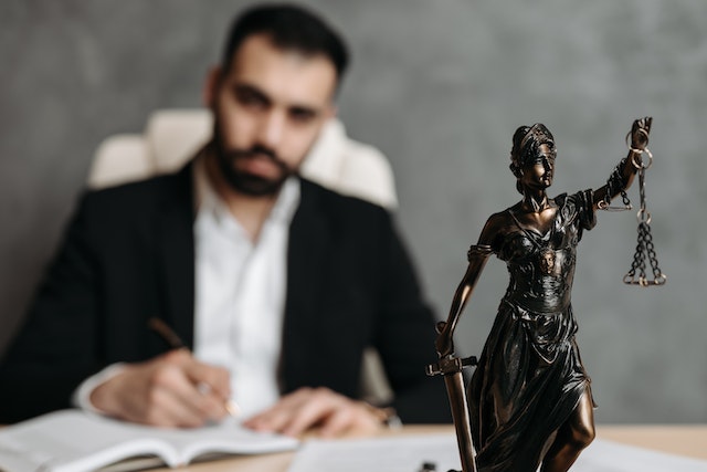 small statue of lady justice on a lawyers desk with the lawyer in the background